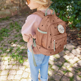 A child standing outside and wearing the Lassig kids mini caramel happy print backpack
