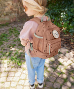 A child standing outside and wearing the Lassig kids mini caramel happy print backpack