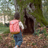 A child walking through leaves near a big tree and wearing the Lassig kids mini advetnure backpack in rose.