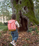 A child walking through leaves near a big tree and wearing the Lassig kids mini advetnure backpack in rose.