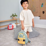 A child in a playroom and holding the Lassig kids tiny digger backpack by the loop handle on the top.