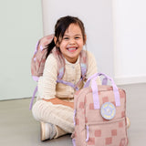 A child sitting on the floor and wearing the Lassig kids mini pattern party rose pattern backpack with another in front.
