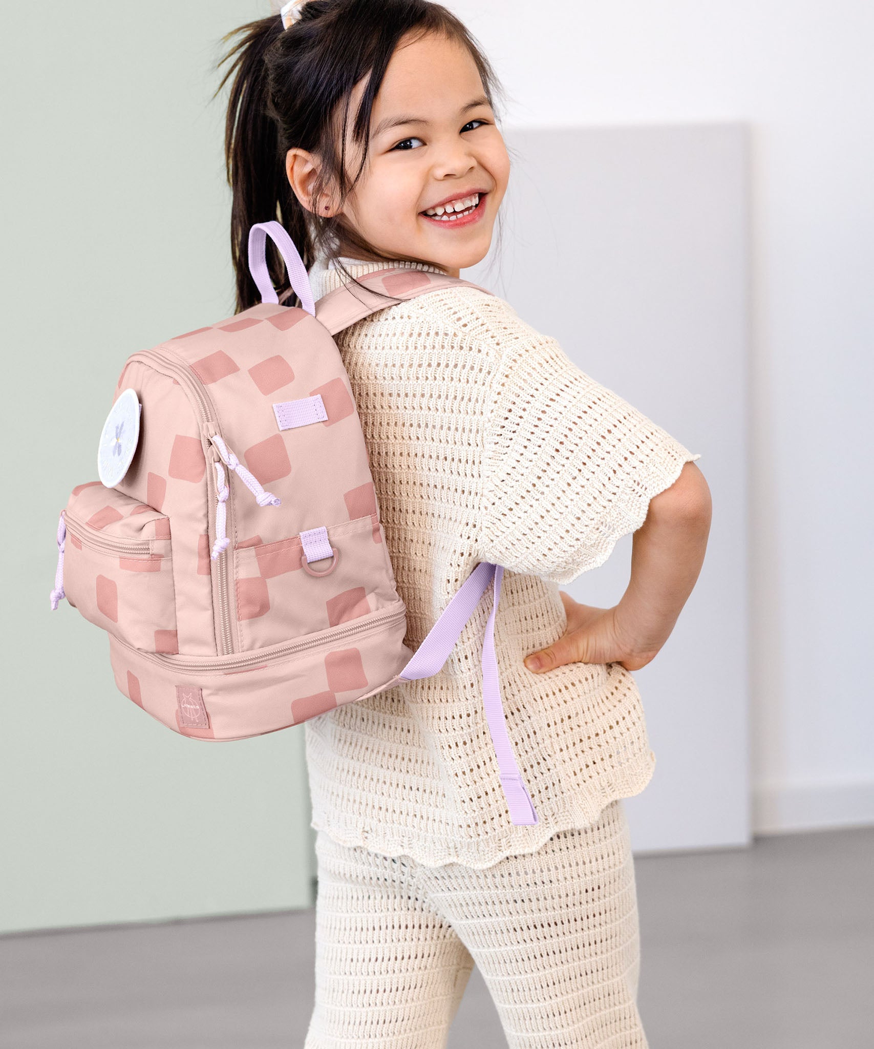 A child posing and wearing the Lassig kids mini pattern party rose pattern backpack.