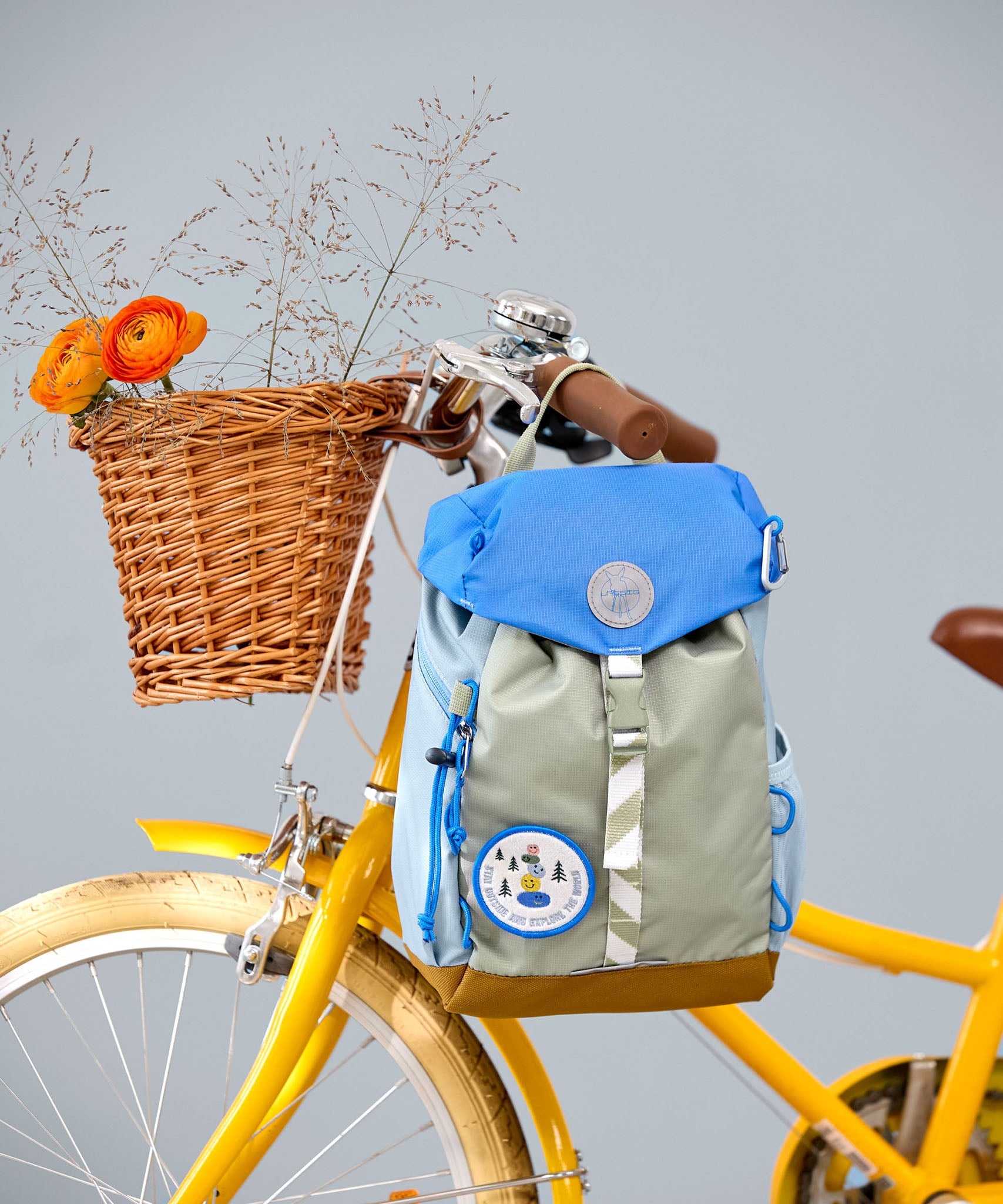 Lassig kids mini outdoor backpack in sunny explorer green hanging on a yellow bicycle.