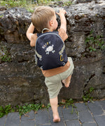 A little boy climbing a wall, wearing the Lassig tiny kids backpack for toddlers and little children, in a dark navy blue.