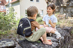 Two children sat on a wall, the boy is wearing the Lassig tiny kids backpack for toddlers and little children, in a dark navy blue.