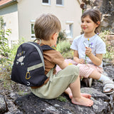 Two children sat on a wall, the boy is wearing the Lassig tiny kids backpack for toddlers and little children, in a dark navy blue.