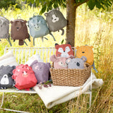 The Lassig 'About Friends' kids tiny backpack range, all laid out on a bench and hanging on a string in a garden. There are many different animal backpacks.