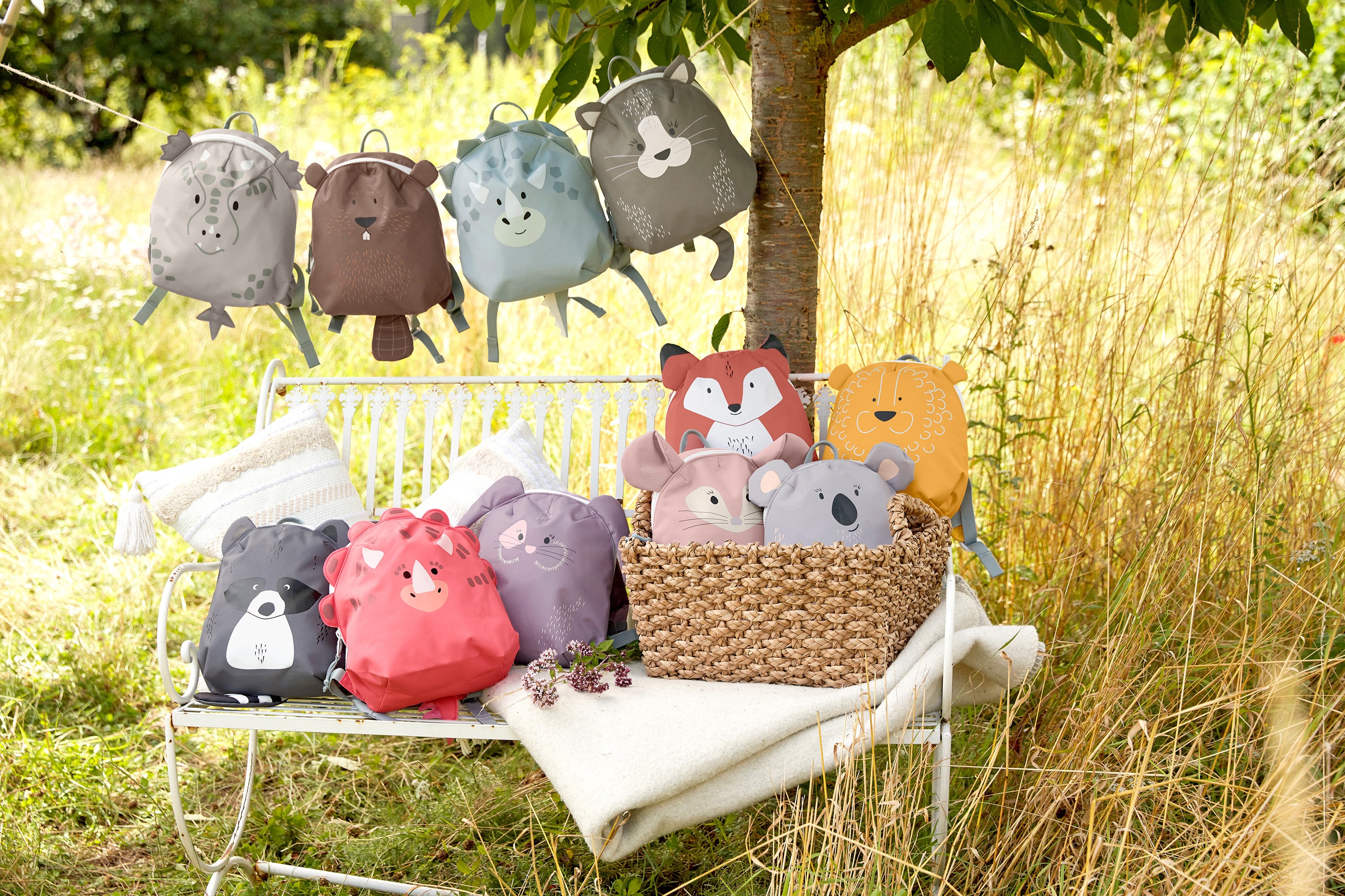 The Lassig 'About Friends' kids tiny backpack range, all laid out on a bench and hanging on a string in a garden. There are many different animal backpacks.