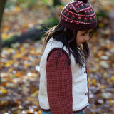 Child wearing an organic knit chocolate brown hat with a red floral pattern, brown pom pom and chin straps, by Little Green Radicals, available now at Babipur.