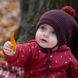 Close up of a baby holding a crispy autumn leaf wearing a knitted chocolate brown pom pom hat, made from soft Fairtrade and GOTS certified organic cotton by Little Green Radicals - available now at Babipur.