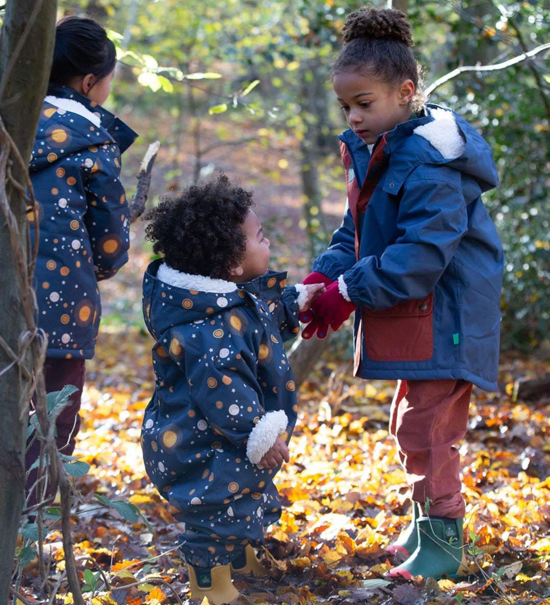 Baby in a forest wearing a Little Green Radicals Waterproof Winter Suit in Night Moon print, blue with stars, made from recycled bottles and a cosy polyester fleece, buy now at Babipur.