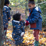 Baby in a forest wearing a Little Green Radicals Waterproof Winter Suit in Night Moon print, blue with stars, made from recycled bottles and a cosy polyester fleece, buy now at Babipur.