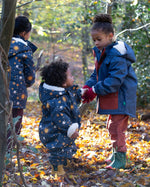 Baby in a forest wearing a Little Green Radicals Waterproof Winter Suit in Night Moon print, blue with stars, made from recycled bottles and a cosy polyester fleece, buy now at Babipur.