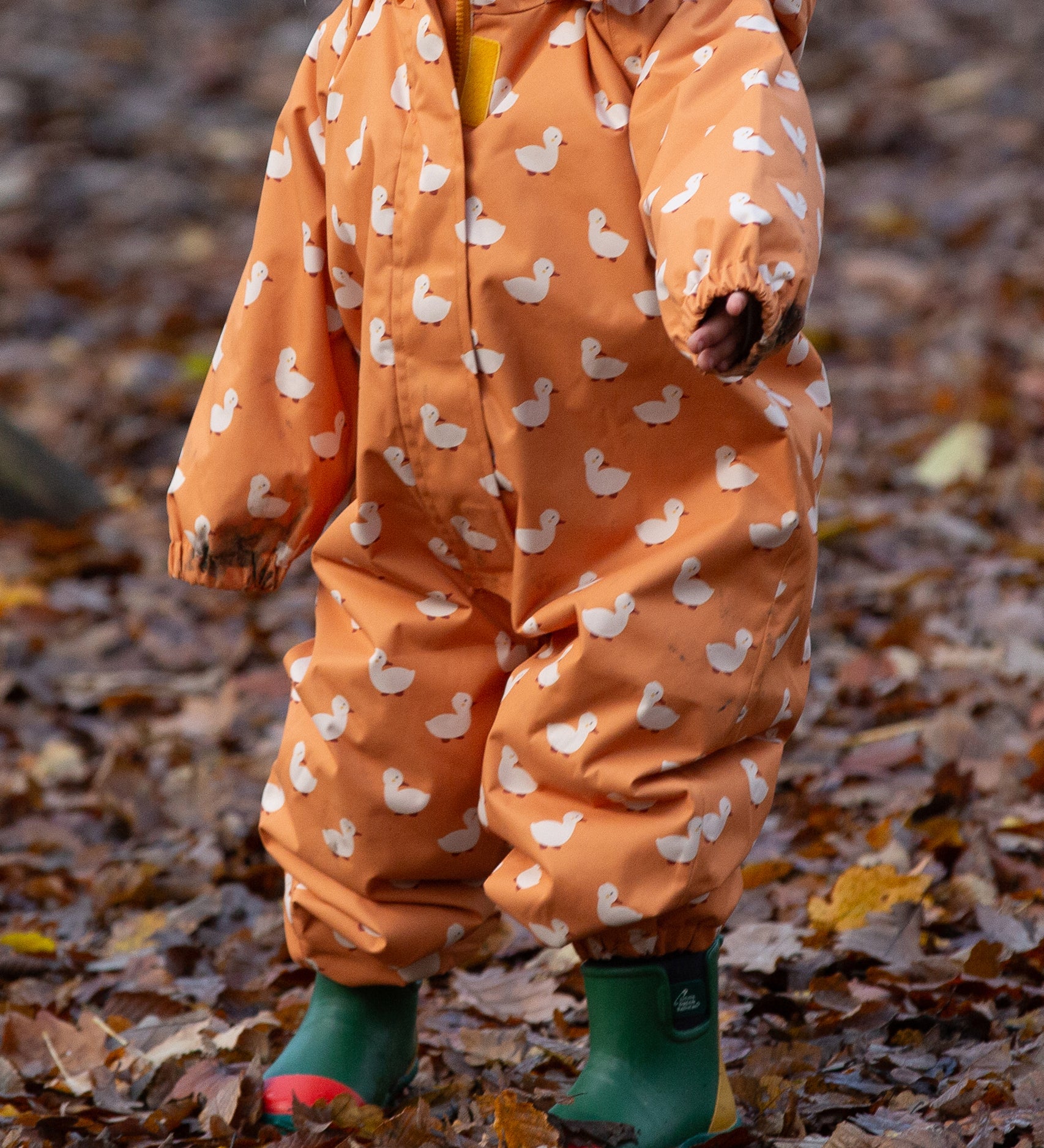 Baby playing in a forest wearing a Waterproof Winter Suit in Gold Ducks print, by Little Green Radicals, made from recycled bottles and a cosy polyester fleece, buy now at Babipur.