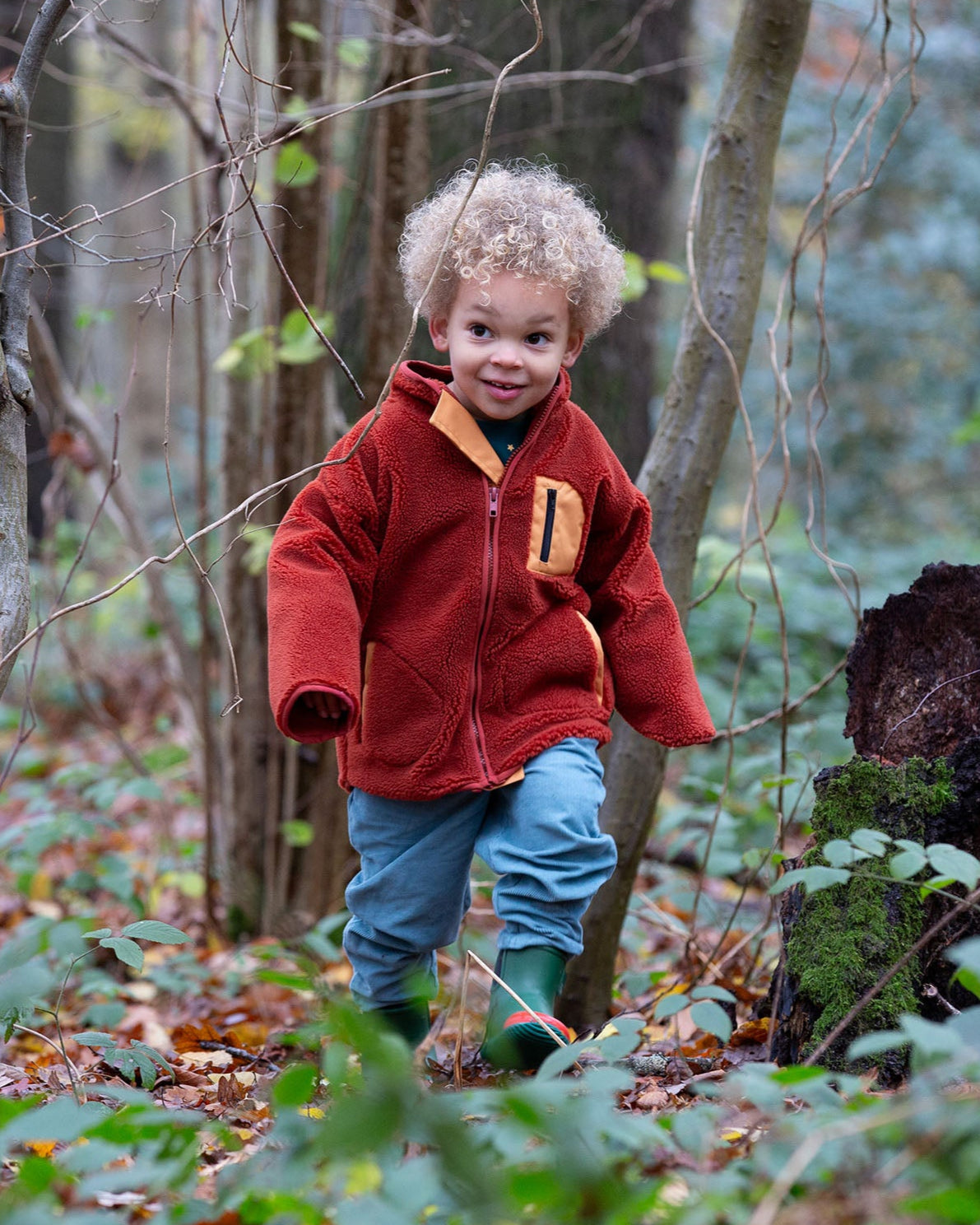 Boy running around a forest wearing Polar Fleece Jacket in ginger red by Little Green Radicals, made from recycled fleece, available now at Babipur.