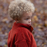 Child playing in a forest wearing Polar Fleece Jacket in Ginger red with yellow zipped pockets by Little Green Radicals, made from recycled fleece, buy now at Babipur.
