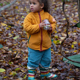 Child playing in a forest wearing Polar Fleece Jacket in Gold with a red zip by Little Green Radicals, made from recycled fleece, buy now at Babipur.