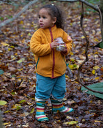 Child playing in a forest wearing Polar Fleece Jacket in Gold with a red zip by Little Green Radicals, made from recycled fleece, buy now at Babipur.