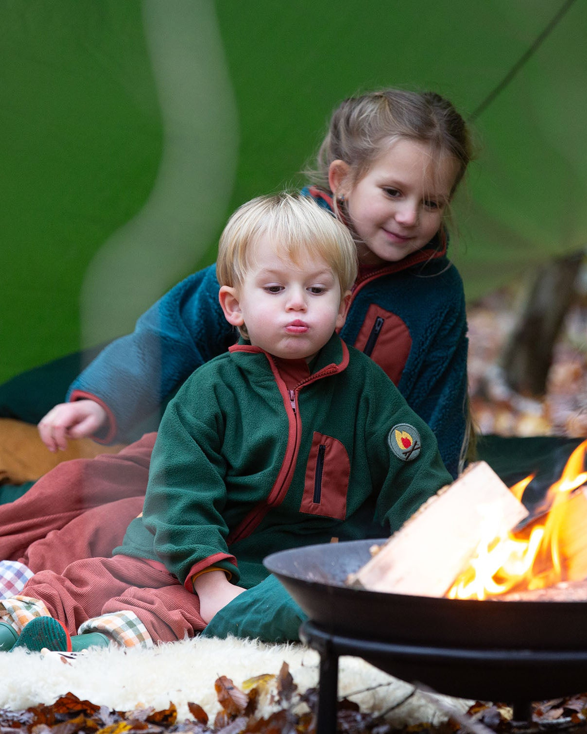 Child sat at a campfire wearing an olive green polar fleece zipped fleece from Little Green Radicals, made from recycled polar fleece, for sale at Babipur.