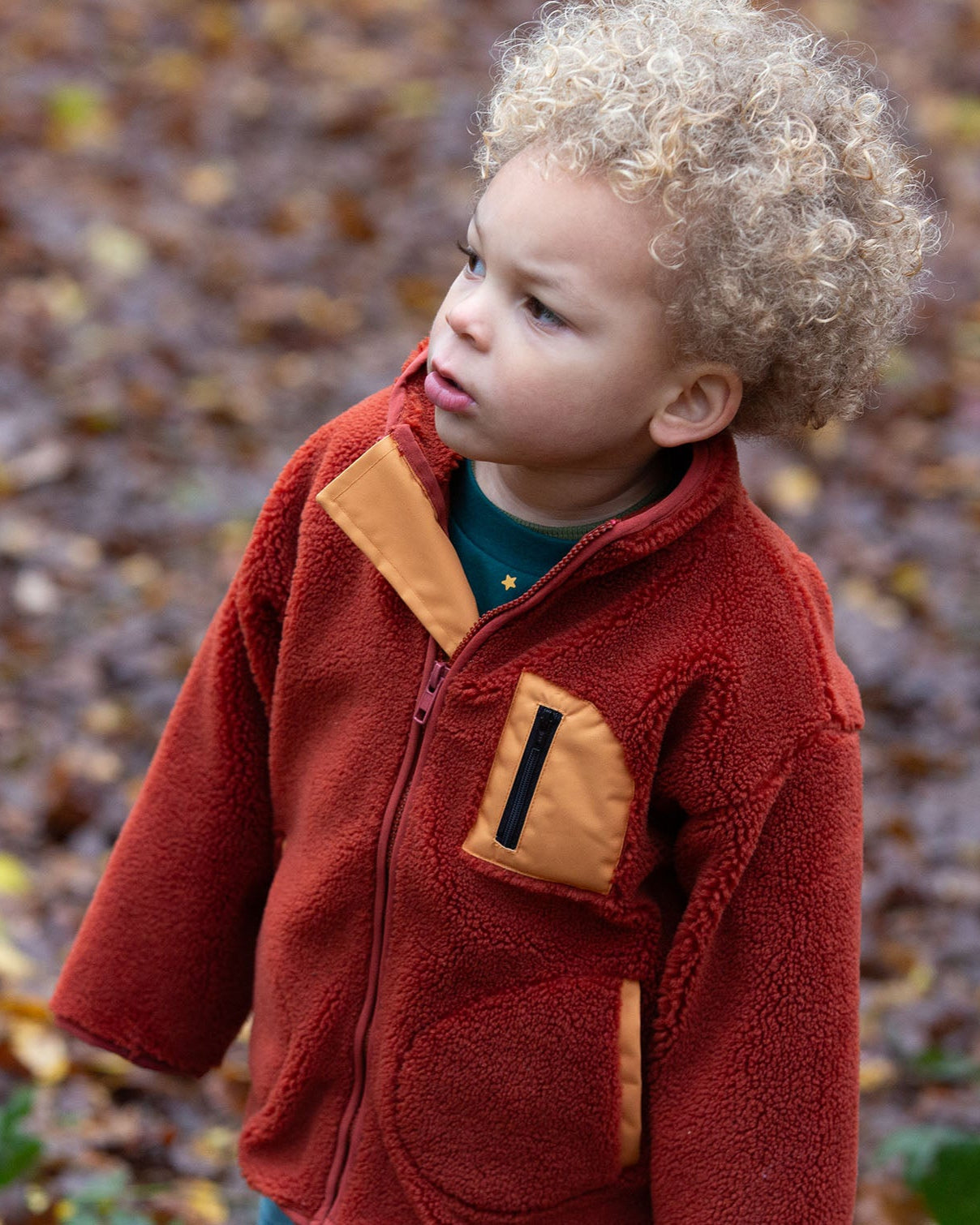 Child in a forest wearing Polar Fleece Jacket in Ginger red with a gold pocket by Little Green Radicals, made from recycled fleece, buy now at Babipur.