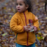Child playing in a forest wearing a yellow gold zipped fleece jacket from Little Green Radicals, made from recycled polar fleece, for sale at Babipur.