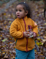 Child playing in a forest wearing a yellow gold zipped fleece jacket from Little Green Radicals, made from recycled polar fleece, for sale at Babipur.