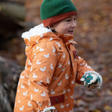 Side view of a child running in a forest wearing a hooded Little Green Radicals Waterproof Winter School Coat, with elasticated sleeves, made from recycled bottles, with a yellow duck print, for sale at Babipur.