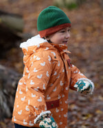 Side view of a child running in a forest wearing a hooded Little Green Radicals Waterproof Winter School Coat, with elasticated sleeves, made from recycled bottles, with a yellow duck print, for sale at Babipur.