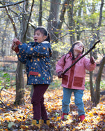 Girl stood in a forest wearing and Waterproof (5000M rating) and warm, PVC free, a cosy hooded kids winter coat by Little Green Radicals, in a Night Moon blue print, with red pockets, available now at Babipur.