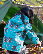 Back of girl playing in a forest wearing a hooded Little Green Radicals Waterproof Winter Coat, made from recycled bottles, with a turquoise Winter Rabbits print, for sale at Babipur.