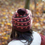 Back of child wearing an organic and Fairtrade knitted chocolate brown hat with a red floral pattern, brown pom pom, by Little Green Radicals, for sale at Babipur.