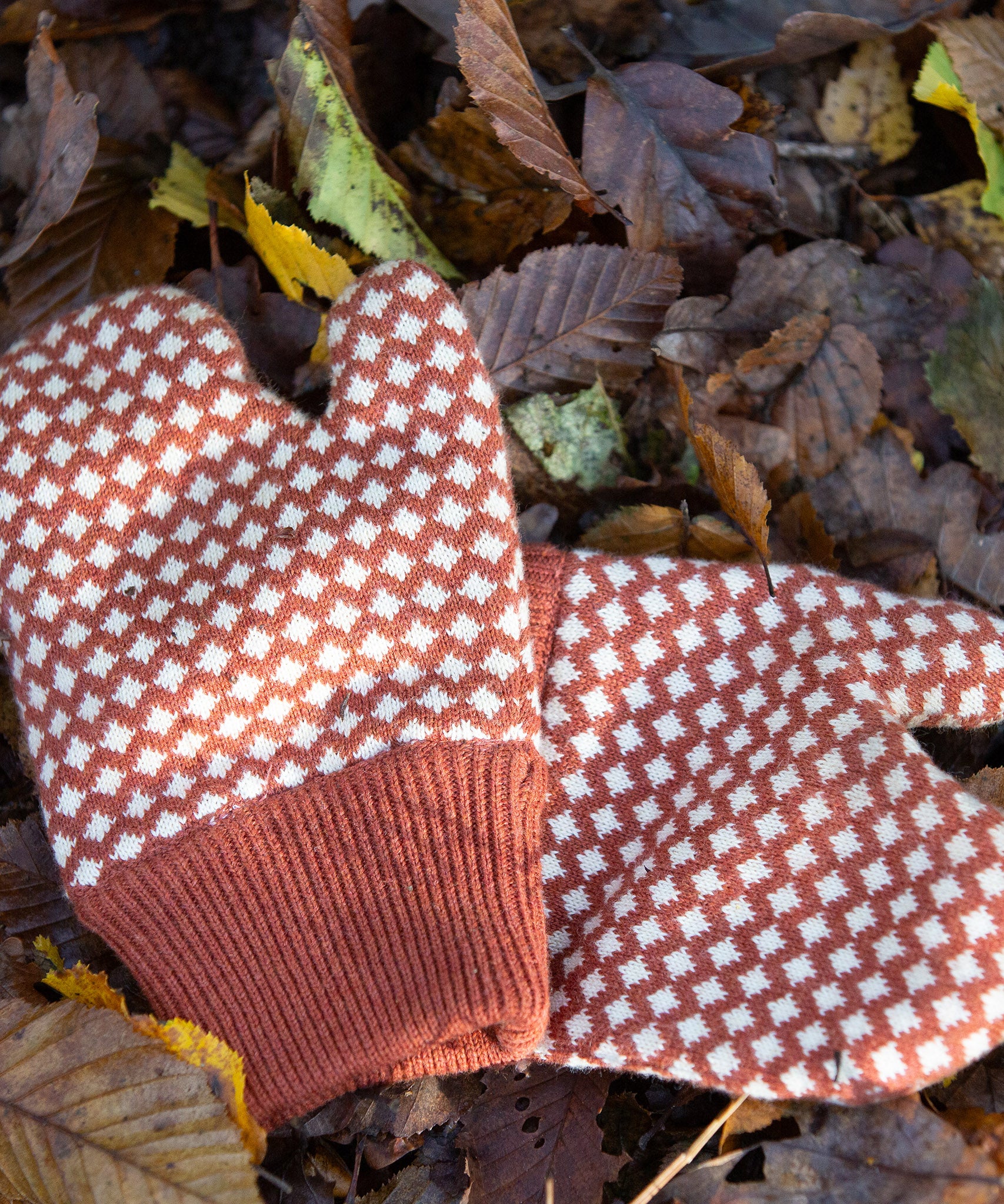 Close up of a pair of Little Green Radicals Knitted Mittens with a Ginger Orange and Cream Diamond Pattern - made from soft Fairtrade certified and GOTS organic cotton - with thick orange cuffs - available to buy at Babipur.