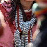 Close up of a child in the forest wrapped in a blue and cream striped knitted scarf from Little Green Radicals, crafted with Fairtrade and GOTS-certified organic cotton, available at Babipur.