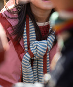 Close up of a child in the forest wrapped in a blue and cream striped knitted scarf from Little Green Radicals, crafted with Fairtrade and GOTS-certified organic cotton, available at Babipur.