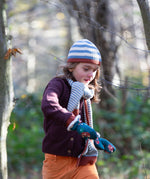 Child running through a forest wearing a striped blue and cream Knit Beanie by Little Green Radicals with a red trim and matching scarf - made from soft GOTS organic and Fairtrade certified cotton - available to buy at Babipur.