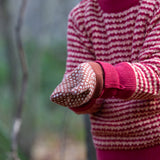 Close up of a child wearing a pair of Little Green Radicals Knitted Mittens with a Ginger Orange and Cream Diamond Pattern and thick orange cuffs - made from soft Fairtrade certified and GOTS organic cotton, for sale at Babipur.