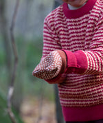 Close up of a child wearing a pair of Little Green Radicals Knitted Mittens with a Ginger Orange and Cream Diamond Pattern and thick orange cuffs - made from soft Fairtrade certified and GOTS organic cotton, for sale at Babipur.