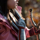 Child in a forest wearing a blue and cream striped knitted scarf by Little Green Radicals - made from Fairtrade and GOTS certified organic cotton, for sale at Babipur.