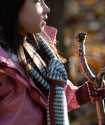 Child in a forest wearing a blue and cream striped knitted scarf by Little Green Radicals - made from Fairtrade and GOTS certified organic cotton, for sale at Babipur.