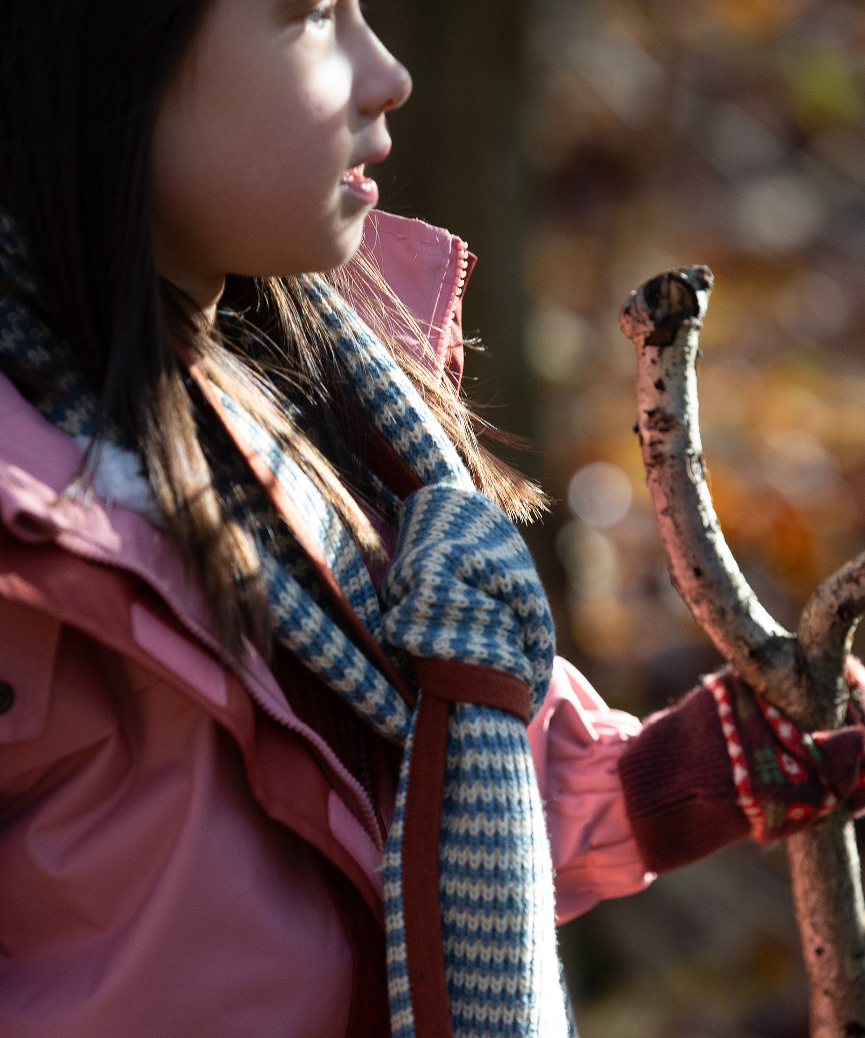 Child in a forest wearing a blue and cream striped knitted scarf by Little Green Radicals - made from Fairtrade and GOTS certified organic cotton, for sale at Babipur.