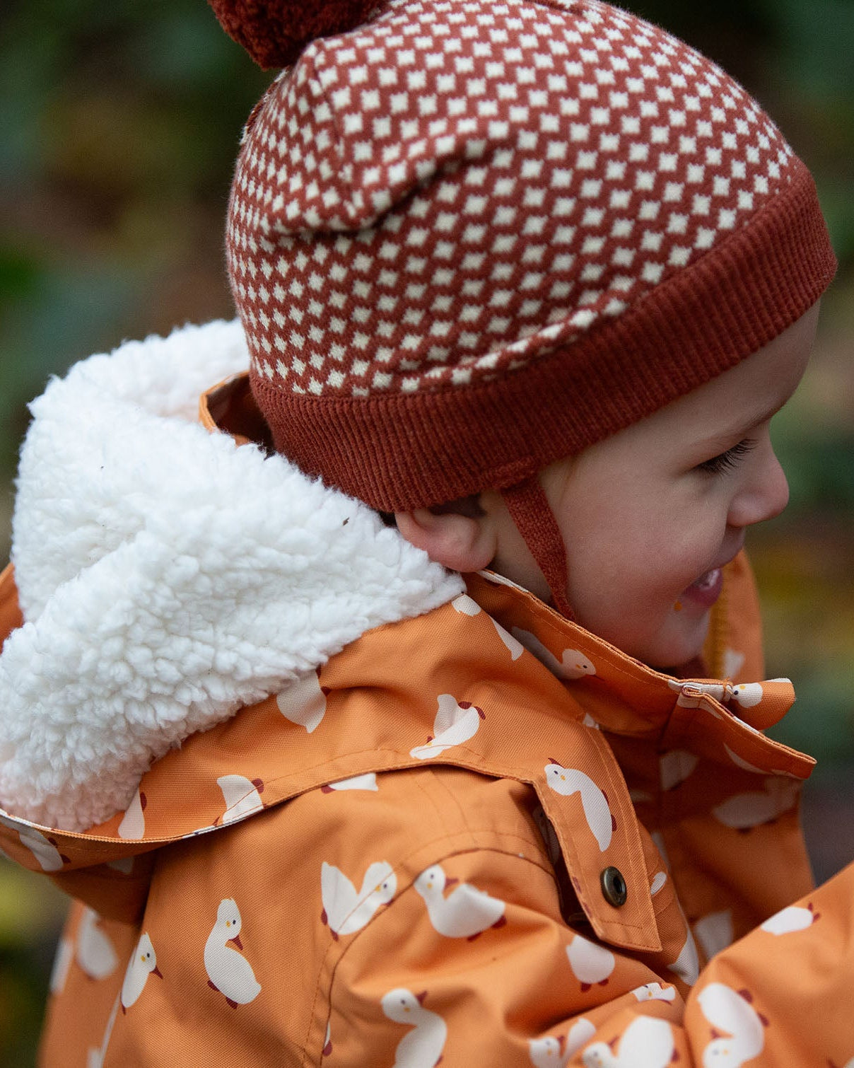 Close up of a child outdoor wearing a Kids Warm Waterproof, 5000MM rating, Winter Hooded School Coat in gold duck print, with a fluffy hood, by Little Green Radicals, made from recycled bottles and a cosy polyester fleece, buy now at Babipur.