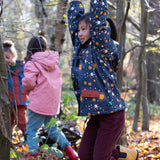 Girl hanging on a tree in a forest, wearing a hooded Little Green Radicals Waterproof Winter School Coat, made from recycled bottles, with a navy night moon print, for sale at Babipur.