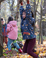 Girl hanging on a tree in a forest, wearing a hooded Little Green Radicals Waterproof Winter School Coat, made from recycled bottles, with a navy night moon print, for sale at Babipur.