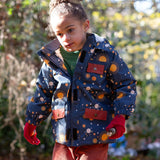 Girl stood in a forest wearing a Warm and Waterproof (5000M rating), PVC free kids school coat by Little Green Radicals, in a navy night moon print, with red front pockets, buy now at Babipur.
