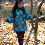 Girl stood in a forest wearing and Waterproof (5000M rating) and warm, PVC free, hooded kids winter coat by Little Green Radicals, in a Winter Rabbit blue print, with red pockets, available now at Babipur.