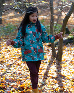 Girl stood in a forest wearing and Waterproof (5000M rating) and warm, PVC free, hooded kids winter coat by Little Green Radicals, in a Winter Rabbit blue print, with red pockets, available now at Babipur.