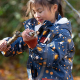 Child in a forest wearing a Little Green Radicals Waterproof Winter Coat in a navy Night Moon print, with a cosy fluffy hood, made from recycled bottles and a cosy polyester fleece, for sale at Babipur.