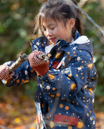 Child in a forest wearing a Little Green Radicals Waterproof Winter Coat in a navy Night Moon print, with a cosy fluffy hood, made from recycled bottles and a cosy polyester fleece, for sale at Babipur.