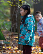 Child in a forest wearing a Little Green Radicals Waterproof Winter Coat in a turquoise Winter Rabbits print, with a cosy fluffy hood, made from recycled bottles and a cosy polyester fleece, for sale at Babipur.